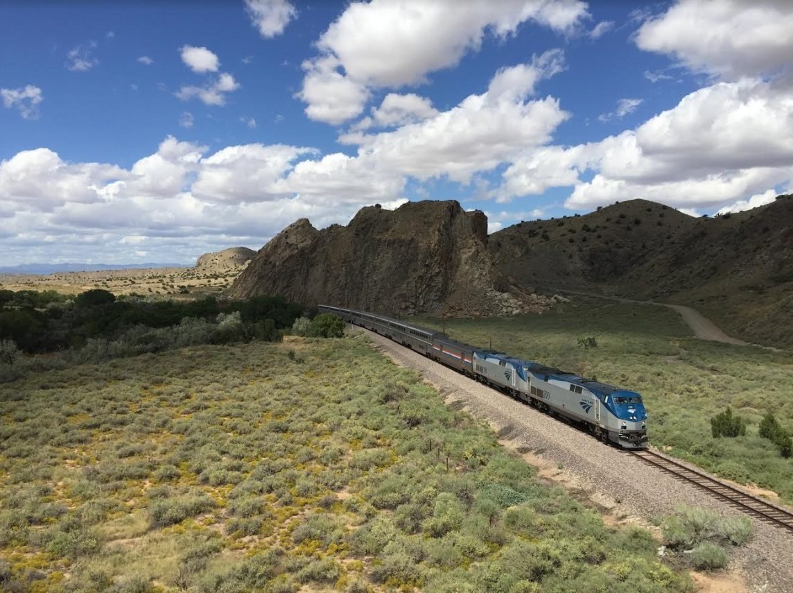 Long-distance passenger train crossing an open high-desert landscape beneath a wide sky