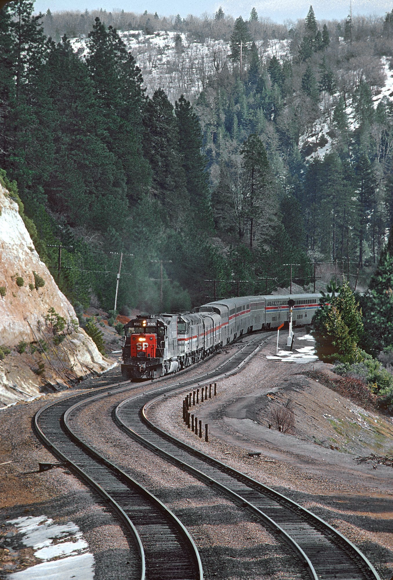 Long-distance passenger train rounding a mountain curve through a snow-dusted forest corridor
